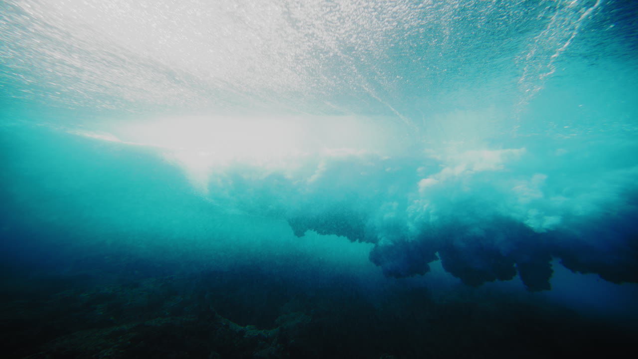 Sun beams sparkle through crystal clear water behind wave at Cloudbreak Fiji