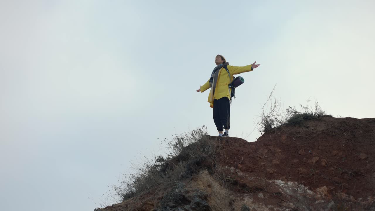 un hombre de pie en la cima de una montaña con las manos extendidas y disfrutando de la vista, vista de bajo ángulo