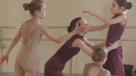 a group of young ballet students in black dancewear practicing positions in a spacious ballet studio with wooden flooring and wall-mounted barres. focused expressions and synchronized movements.