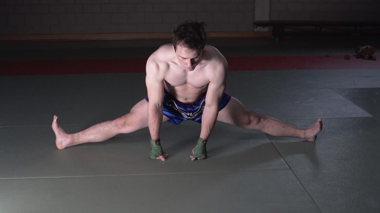 Kickboxer strechting his legs in to a split and focussing on his breathing