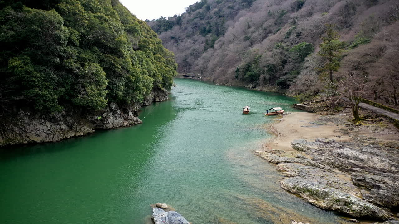 disparo cinematográfico de drones bajando por un río pasando pequeños botes en kioto, japón