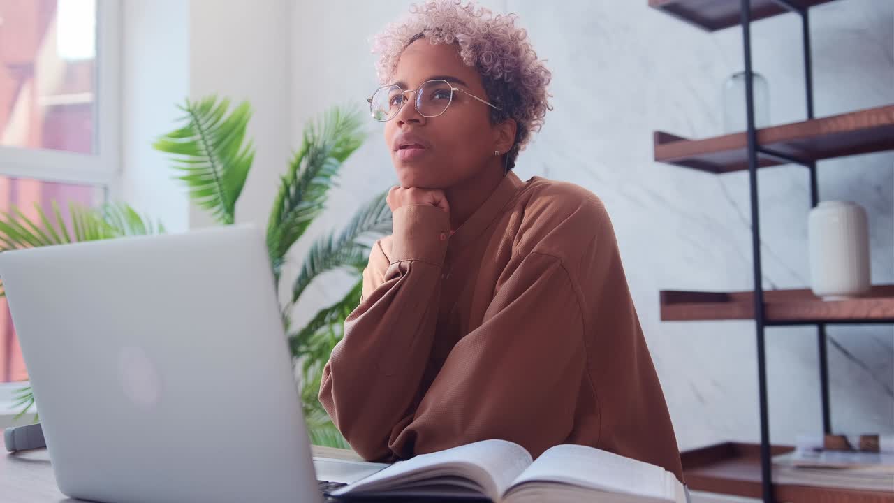 Dark skinned woman dreams of something while sitting on laptop in office
