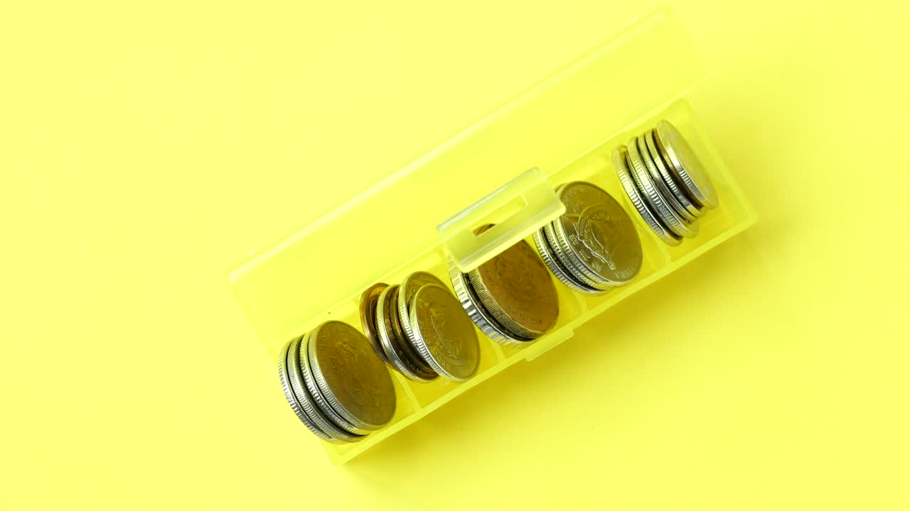 Close up of coins in a plastic box on yellow background