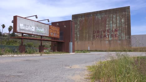 establishing shot of an abandoned drive in movie theater with man on harley motorcyle passing