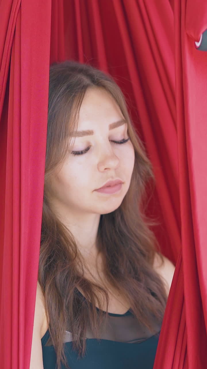 concentrated woman relaxes in red hammock after fly yoga workout against blurred women group close view