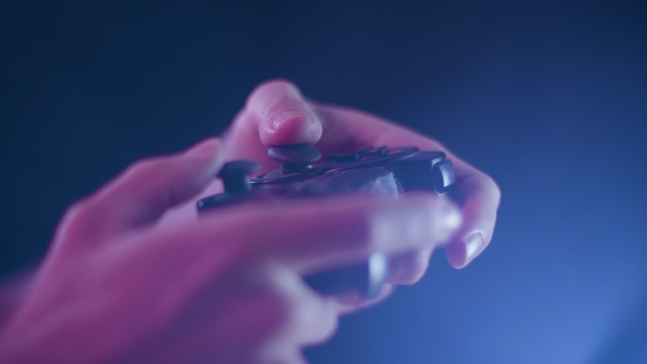 Playing video games on a small controller using joysticks playing quickly with blue lens flare black background