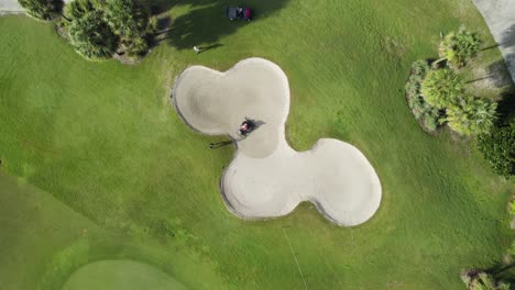 aerial drone shot of golf course bunker being raked by landscaping crew