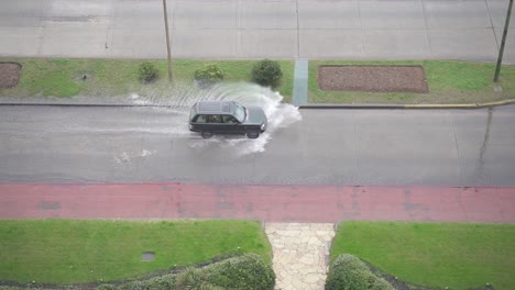 SUV-driving-on-flooded-roads-and-splashing-the-water,-handheld-high-angle