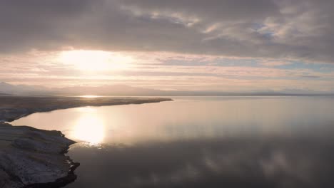 asombrosa puesta de sol sobre montañas nevadas a lo lejos, sobre tranquilas aguas oceánicas islandesas, antena de drones