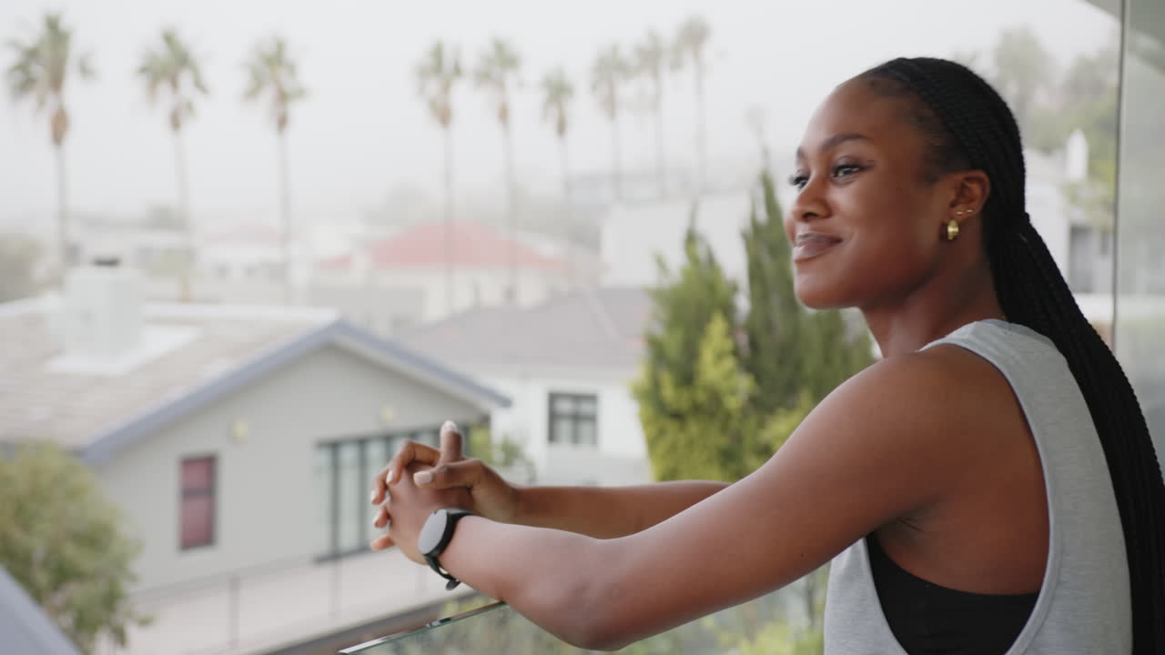 Smiling african american woman leaning on balcony railing, view of neighborhood, copy space