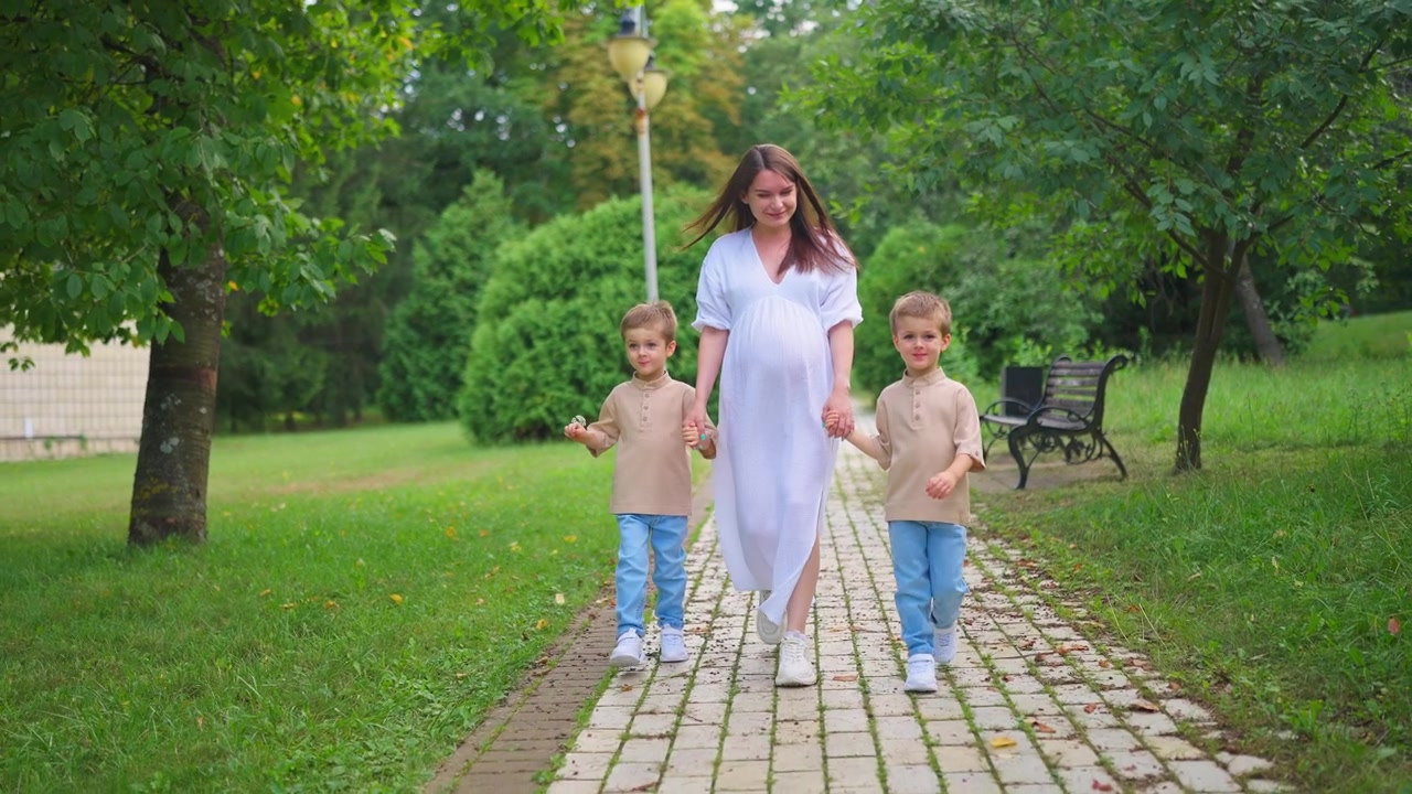 Zwangere vrouw wandelt met twee jonge zonen in een groen park.