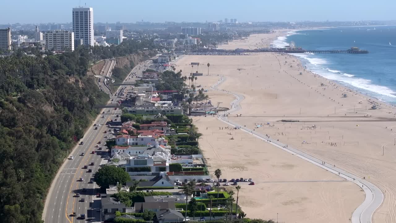 Large beach front Houses In Santa Monica along highway 101 on an overcast day with famous pier off in a distance, 4K Drone Flyover