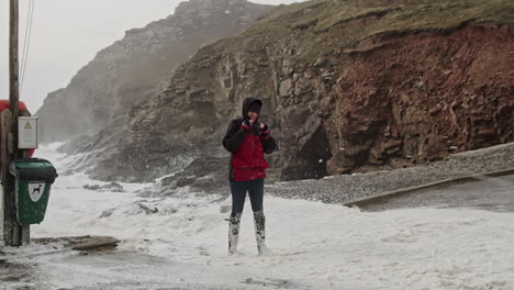 Girl-In-Hooded-Jacket-And-Rubber-Boots-Puts-On-Glasses-During-Storm-Eunice-At-Chapel-Porth-Beach-In-Cornwall-At-Winter