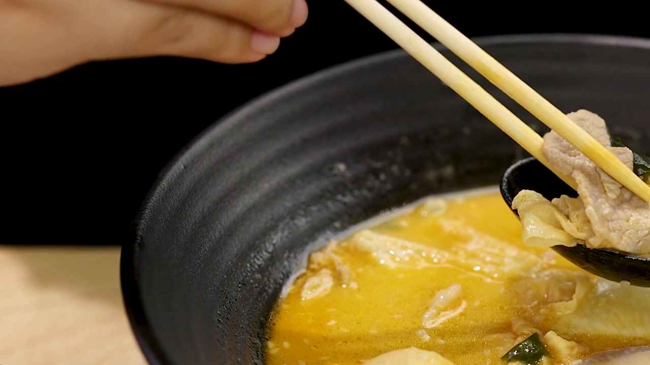 Primo piano di mani che usano le bacchette per sollevare carne di maiale da un brodo giallo piccante