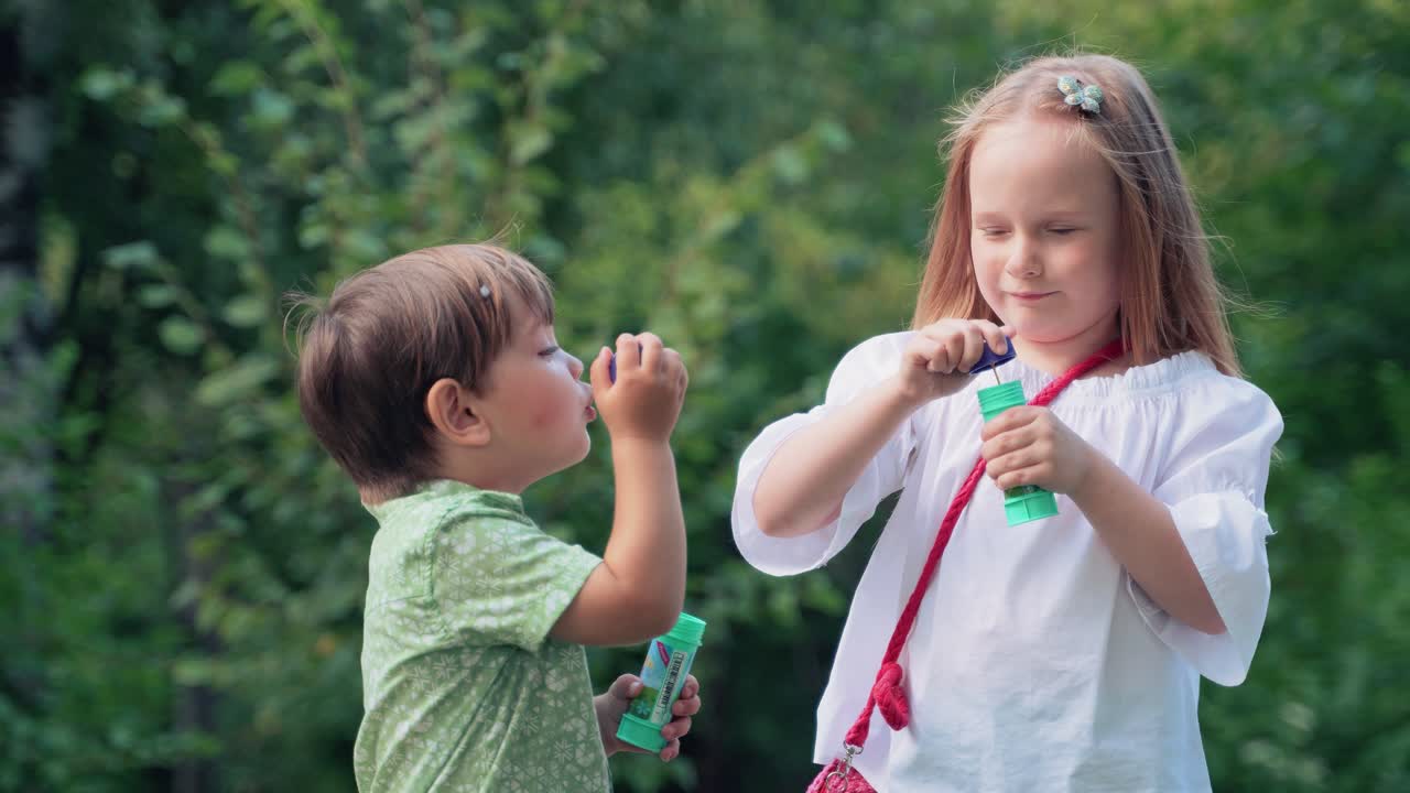 Menino e menina alegres brincam com bolhas de sabão no parque. Crianças sopram bolhas. Jogos ao ar livre.