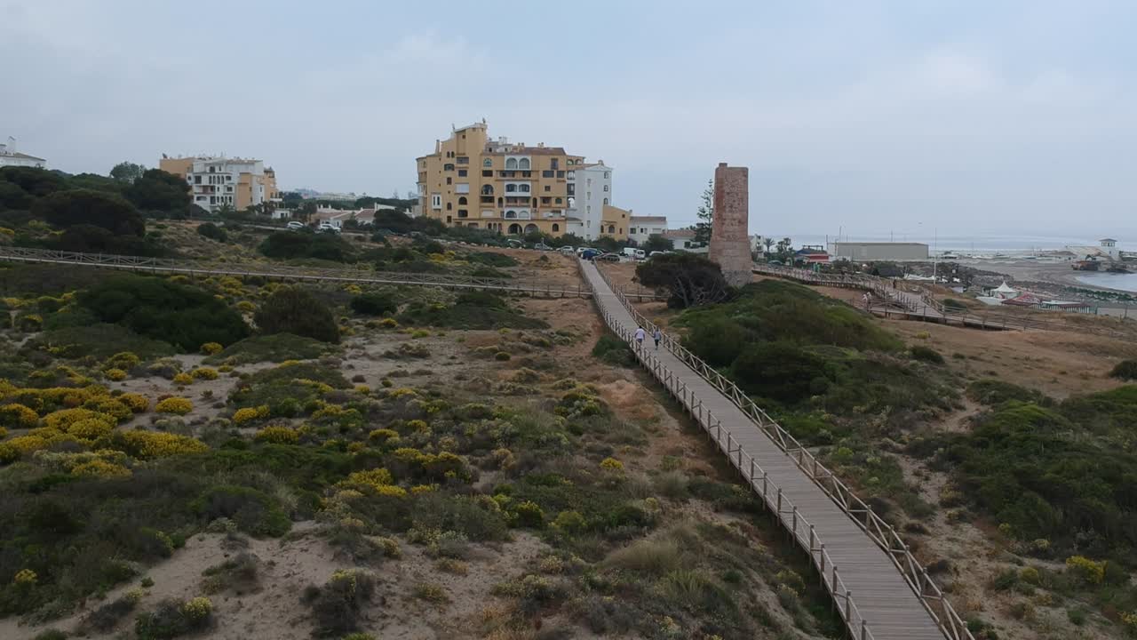 caminos de madera en una playa tranquila con gente paseando por el camino en un pueblo costero en málaga, españa