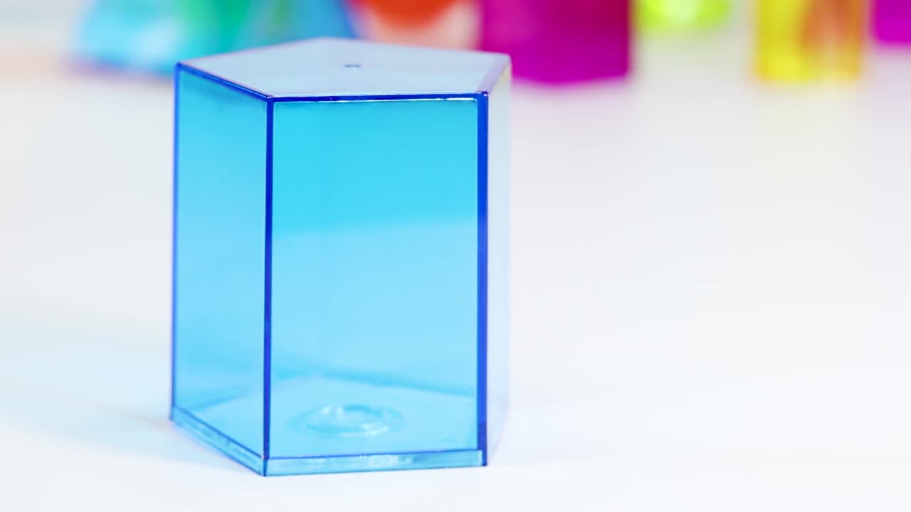 Primo piano di una mano che posiziona un prisma esagonale di plastica blu traslucida su un tavolo.