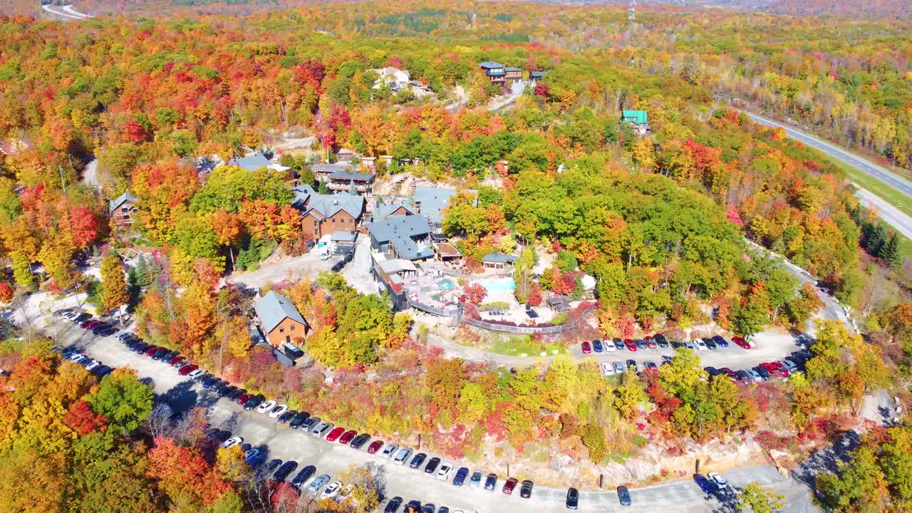 An aerial view reveals a stunning forest with vibrant autumn colors, alongside parking places and cozy vacation houses. The scene captures the perfect getaway, blending nature with relaxation.
