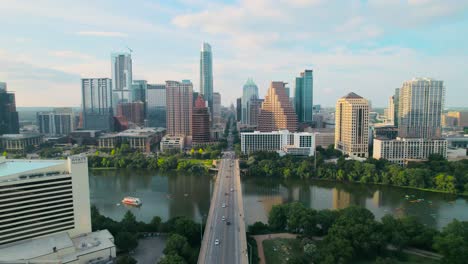 Toma-Aérea-Con-Drones-Del-Emblemático-Puente-De-La-Avenida-Del-Congreso-De-Austin-Y-Del-Capitolio-Del-Estado-De-Texas-Con-Vistas-Al-Centro-De-La-Ciudad-Sobre-El-Río-Colorado-Al-Atardecer,-Con-Automóviles,-Ciclistas-Y-Practicantes-De-Remo-En-El-Río