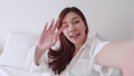 Beautiful-Asian-woman-with-white-shirt-talking-to-selfie-video-call-walk-to-bed-with-a-smile