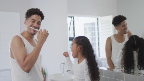 Happy-biracial-father-and-daughter-washing-teeth-in-bathroom-together