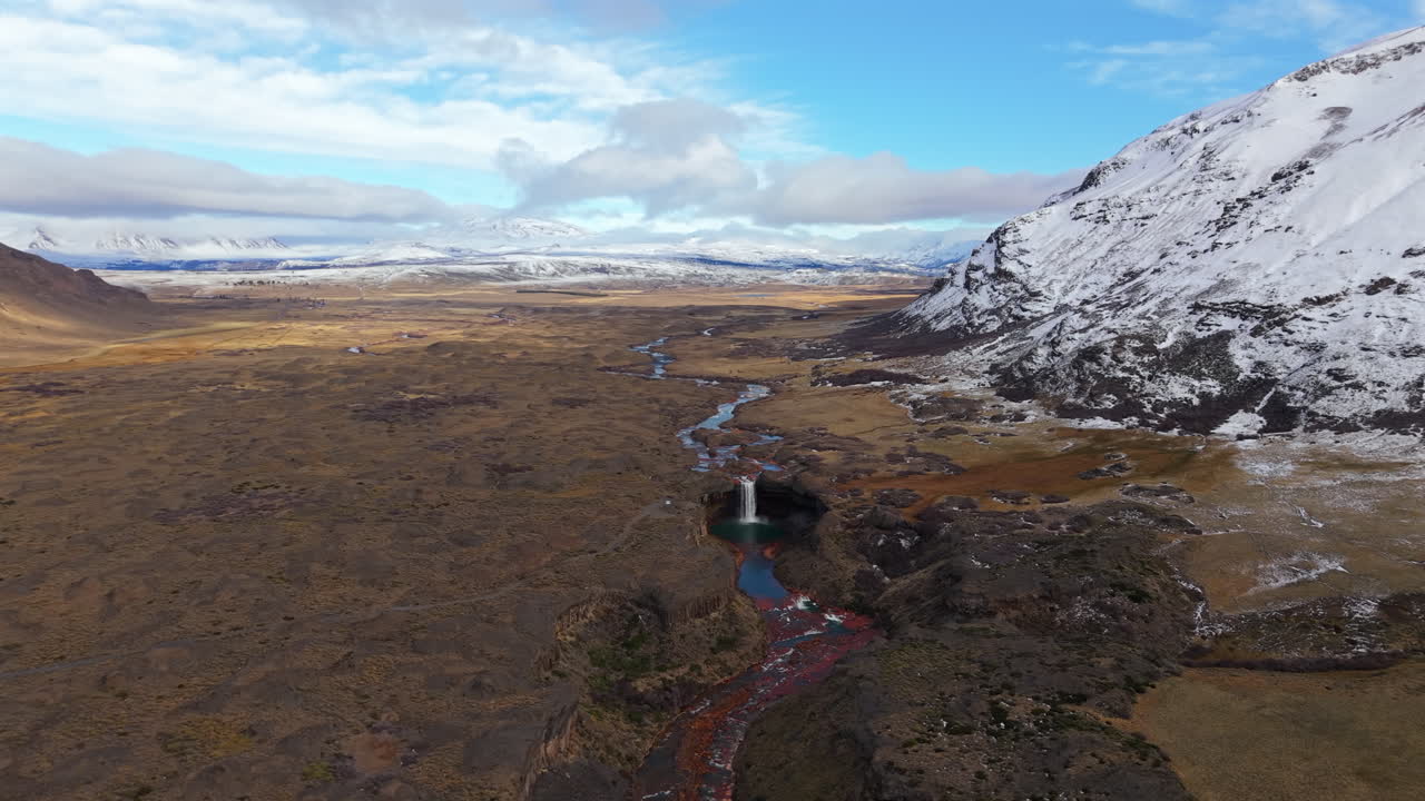 Agrio River winding through a volcanic plateau before plunging into Salto del Agrio, framed by snowy Andean slopes in Neuquén Province, Argentina, High-altitude aerial revealing shot
