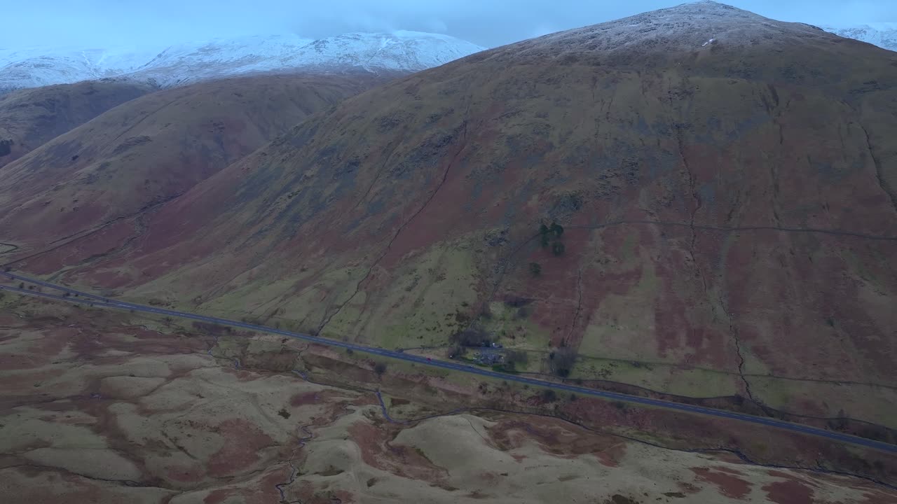 Flight towards mountain road and snow dusted mountains. Lake District, Cumbria, UK.