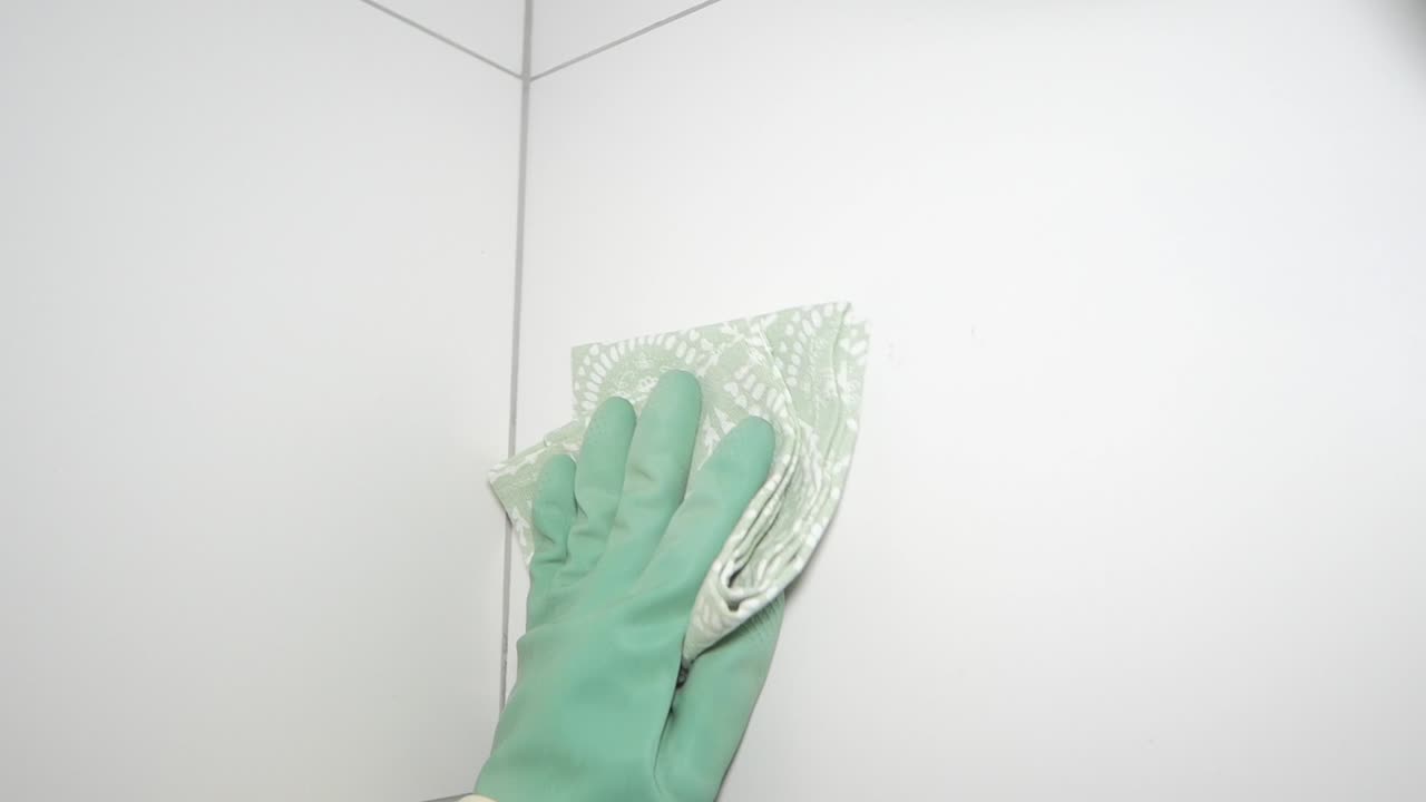 Gloved Hand Wiping a White Tiled Wall