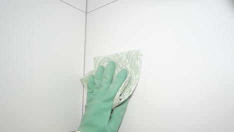 gloved hand wiping a white tiled wall