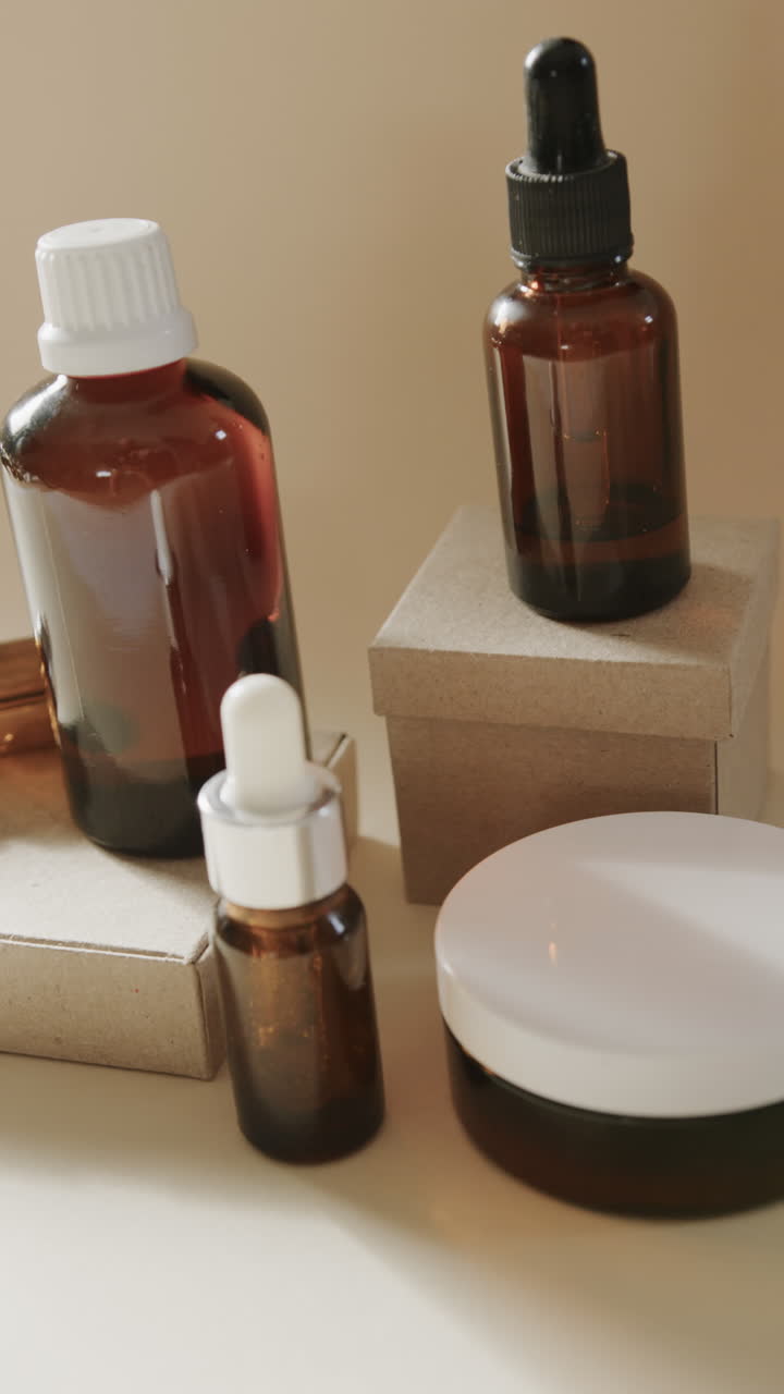 Vertical video of close up of glass bottles with cream and boxes and copy space on beige background