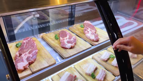 a person selects raw pork cuts from a display case under bright lighting, preparing for a korean bbq experience in bangkok