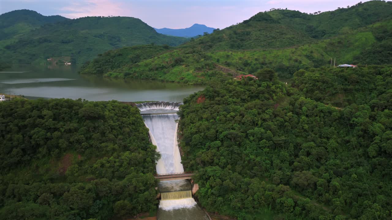 Drone video capturing the serene landscape of Presa EL Carrizo, nestled in lush green hills at sunset. The sweeping aerial view offers a majestic look at the dam and reservoir
