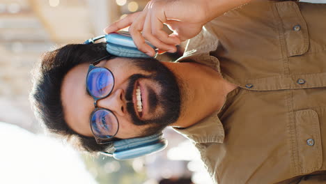 happy young adult man in wireless headphones choosing listening music dancing outdoors city street