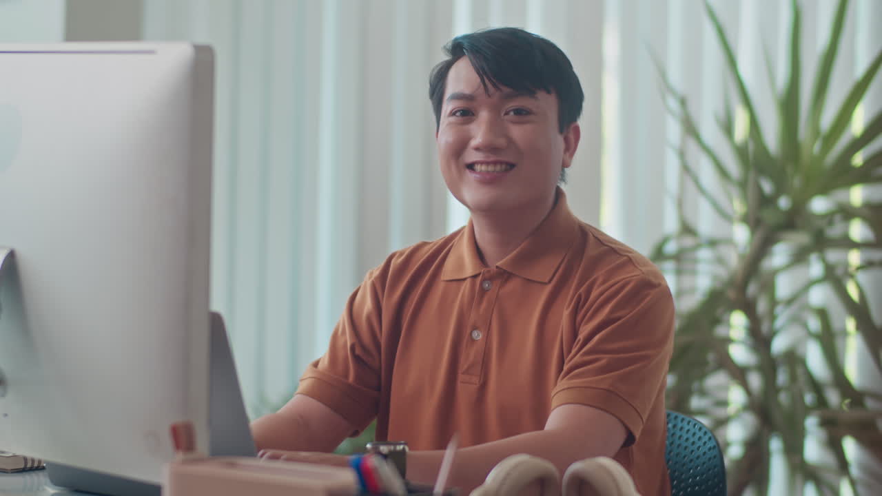 Asian Office Employee Smiling at Camera in front of Monitor