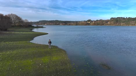 photographer with his camera on tripod near scenic lake - drone pullback