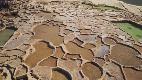 Reverse-Dolly,-Niedrige-Luftaufnahme-Von-Salzpfannen-An-Der-Küste-Der-Insel-Gozo,-Malta