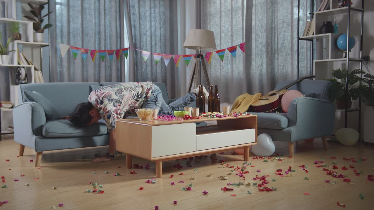 술에 취한 아시아 남자가 소파에서 잠을 자고 집에 있는 파티 에서 두통으로 인해 머리를 손으로 잡고 깨어난다.