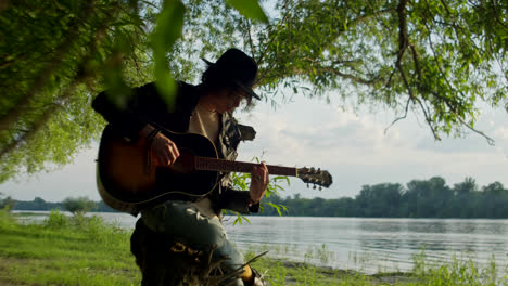man playing acoustic guitar by a river