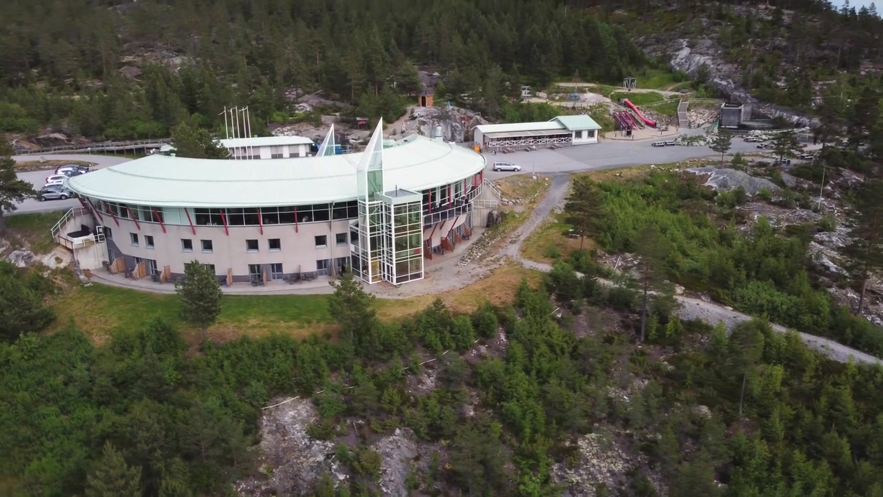 Un moderno hotel in collina con una torre in vetro, circondato da una fitta foresta e terreno roccioso, che offre viste panoramiche e sentieri escursionistici in un tranquillo contesto naturale nordico. Hotel High Coast in Svezia
