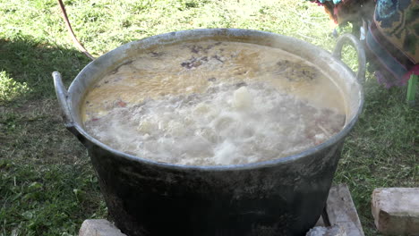 cooking traditional soup in a large cauldron, on a open air -slow motion