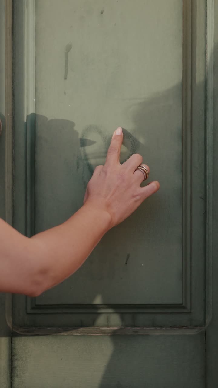 Finger drawing heart shape on dusty door surface with visible texture