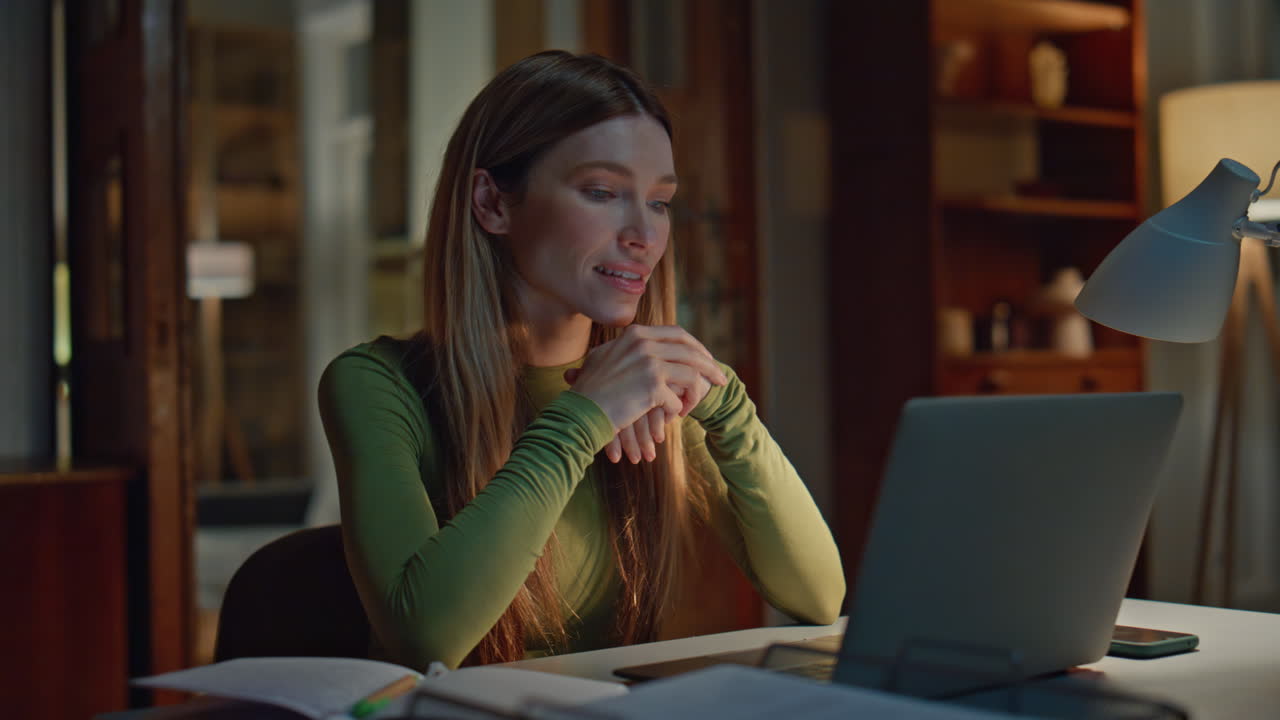 Tutor online che parla in una chat webcam al computer portatile in un appartamento di sera, primo piano.
