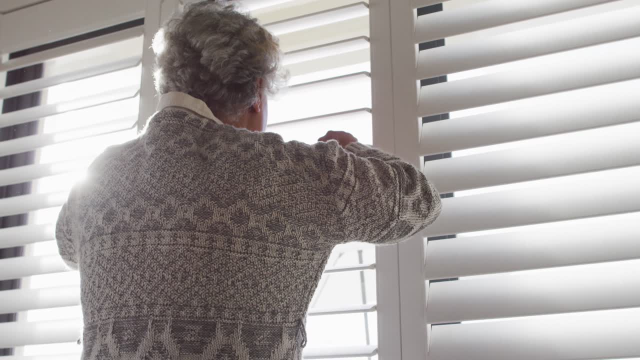 Vista traseira de mulher idosa afro-americana olhando pela janela em casa