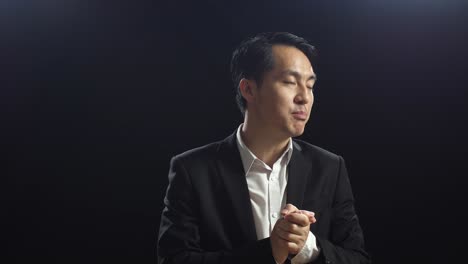 close up of asian speaker man in business suit holding his hands together while speaking in the black screen studio