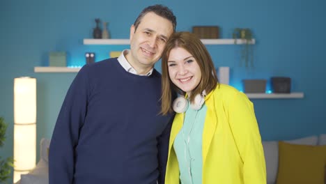 padre e hija de pie en casa mirando a la cámara y riendo.