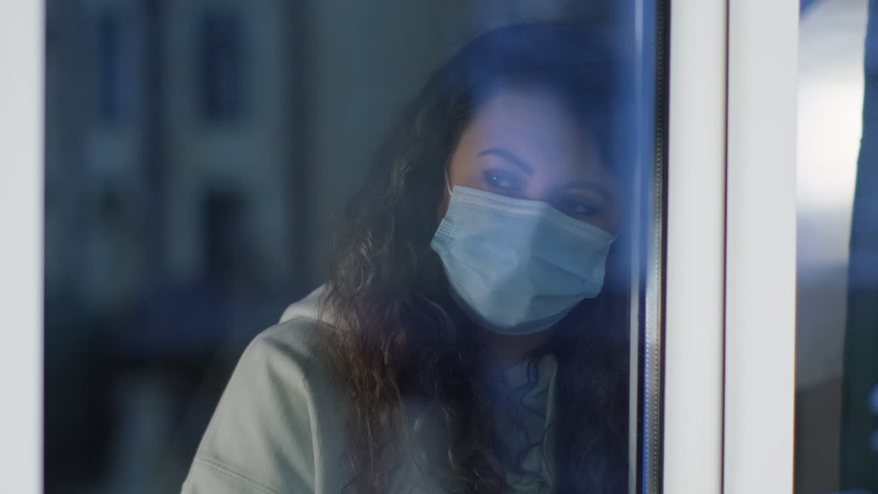 Woman looking out window wearing a mask