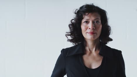 portrait of determined mature businesswoman in suit standing against white studio wall