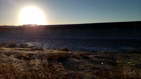 North-Texas-lake-flowing-over-spillway-at-sunset-with-blowing-grass-and-waves-in-the-water