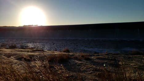 north texas lake flowing over spillway at sunset with blowing grass and waves in the water