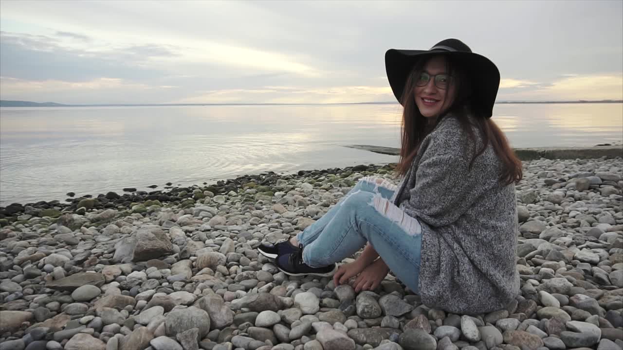 Woman Sitting on a Pebble Beach at Sunset